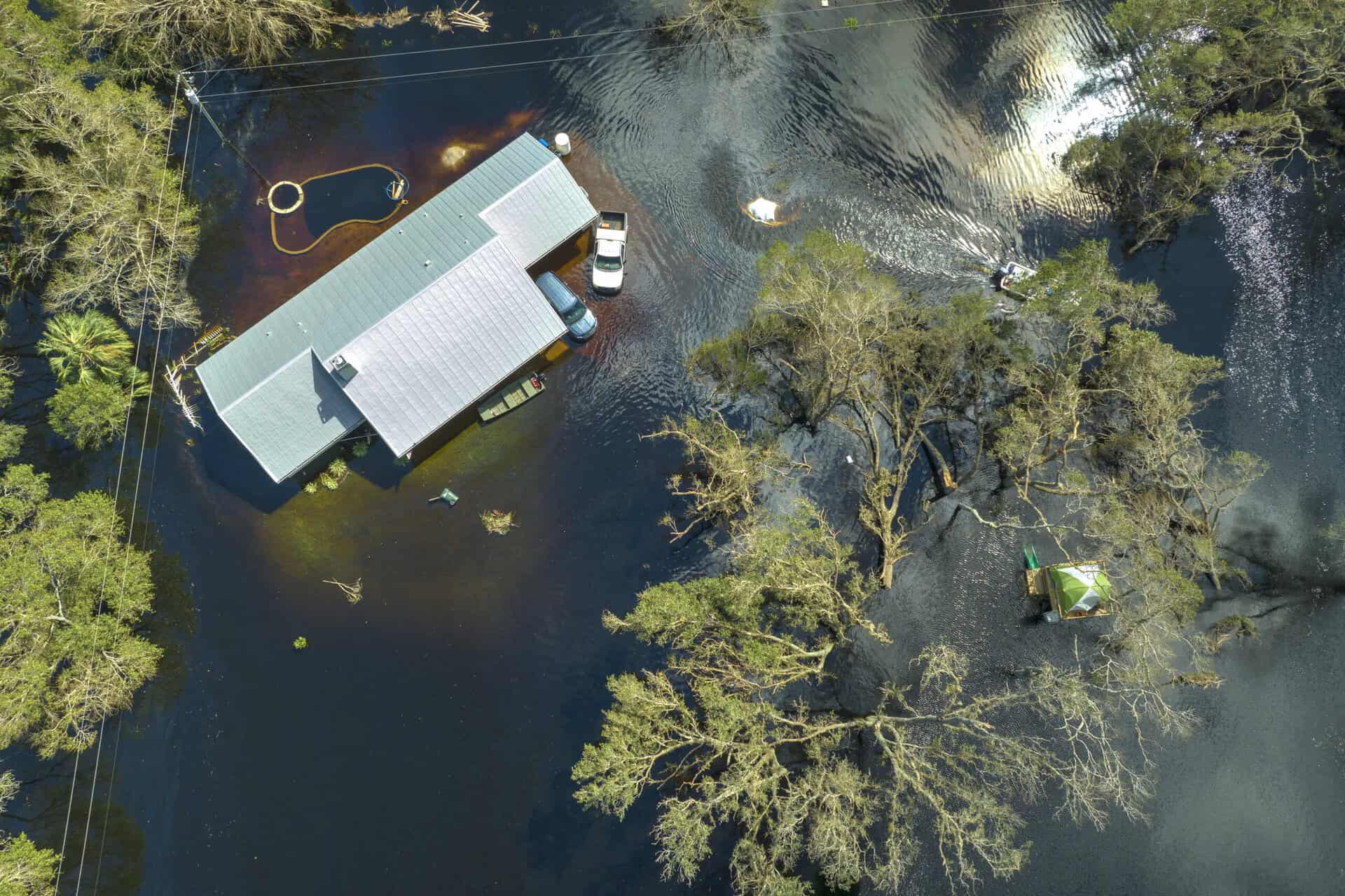 Flooded property with water surrounding the house and trees, highlighting flood risk.