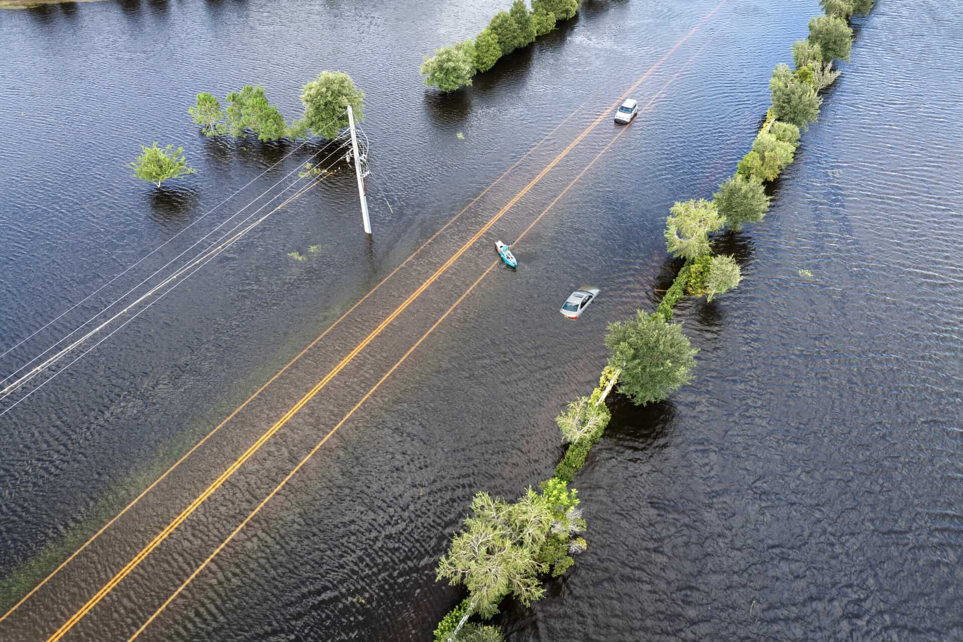 Flooded road with submerged trees and vehicles, highlighting flood risk and insurance needs.