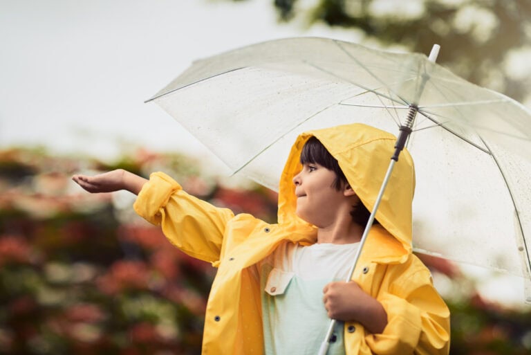 Child in yellow raincoat with umbrella, preparing for flood risk or storm.